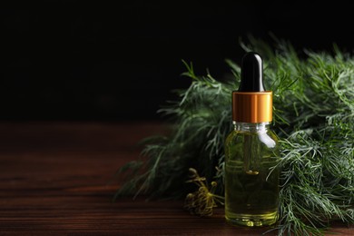 Photo of Bottle of essential oil and fresh dill on wooden table against dark background, closeup. Space for text