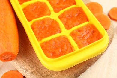 Photo of Carrot puree in ice cube tray and fresh carrot on wooden table, closeup