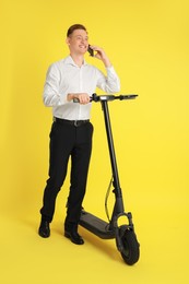 Photo of Happy man with modern electric kick scooter talking on smartphone on yellow background