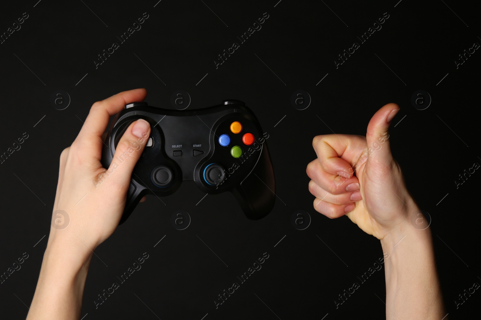 Photo of Woman with game controller showing thumbs up on black background, closeup