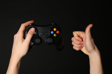 Woman with game controller showing thumbs up on black background, closeup