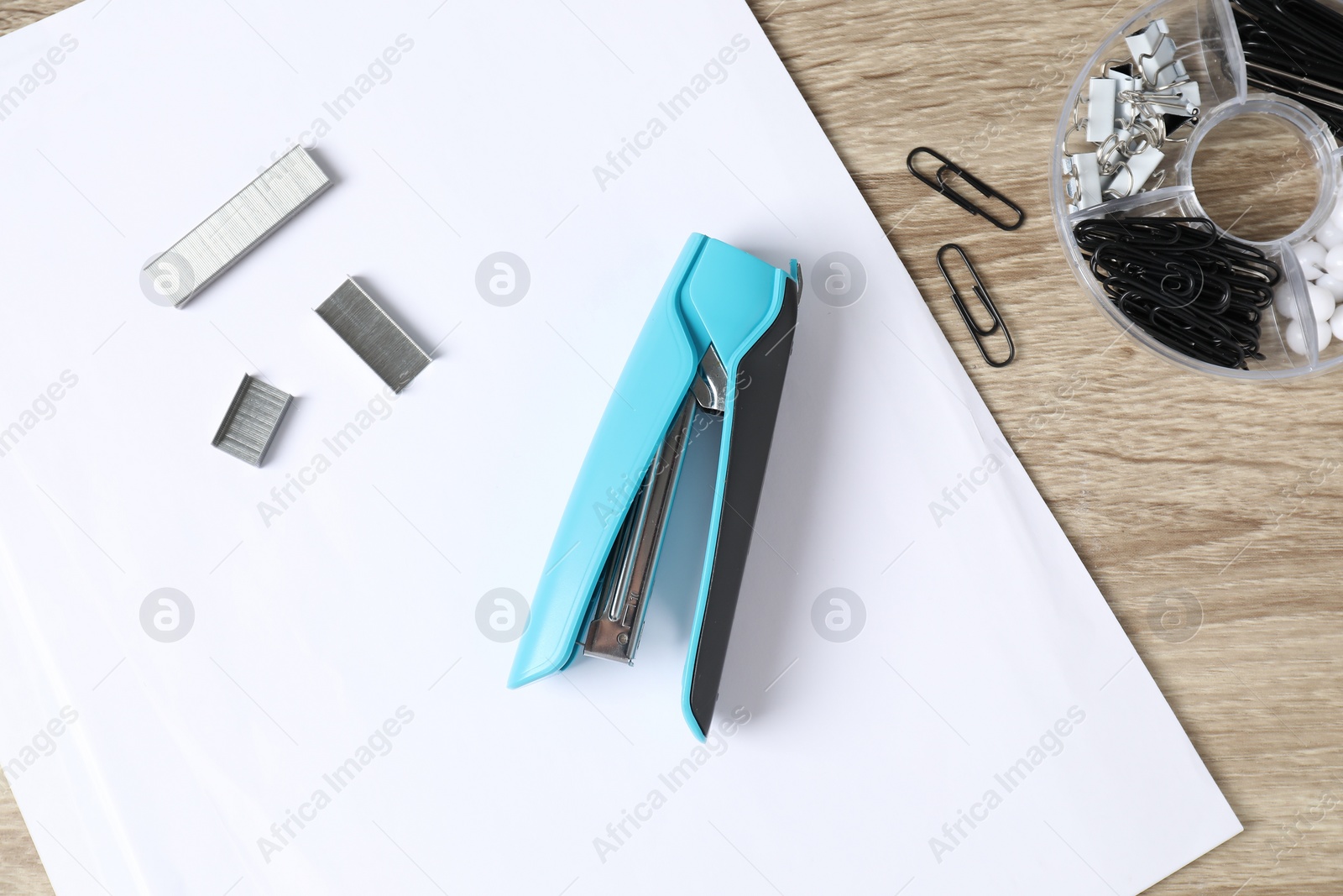 Photo of Stapler, metal staples and different paper clips on wooden table, flat lay