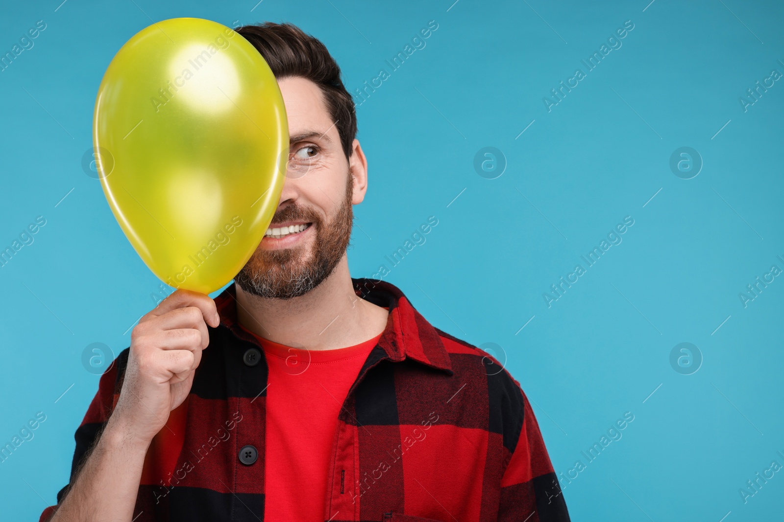 Photo of Happy man with yellow balloon on light blue background. Space for text