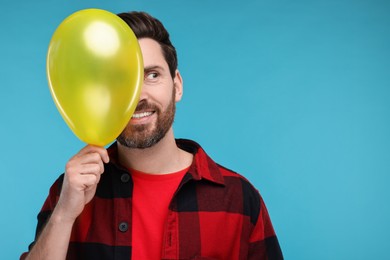 Happy man with yellow balloon on light blue background. Space for text