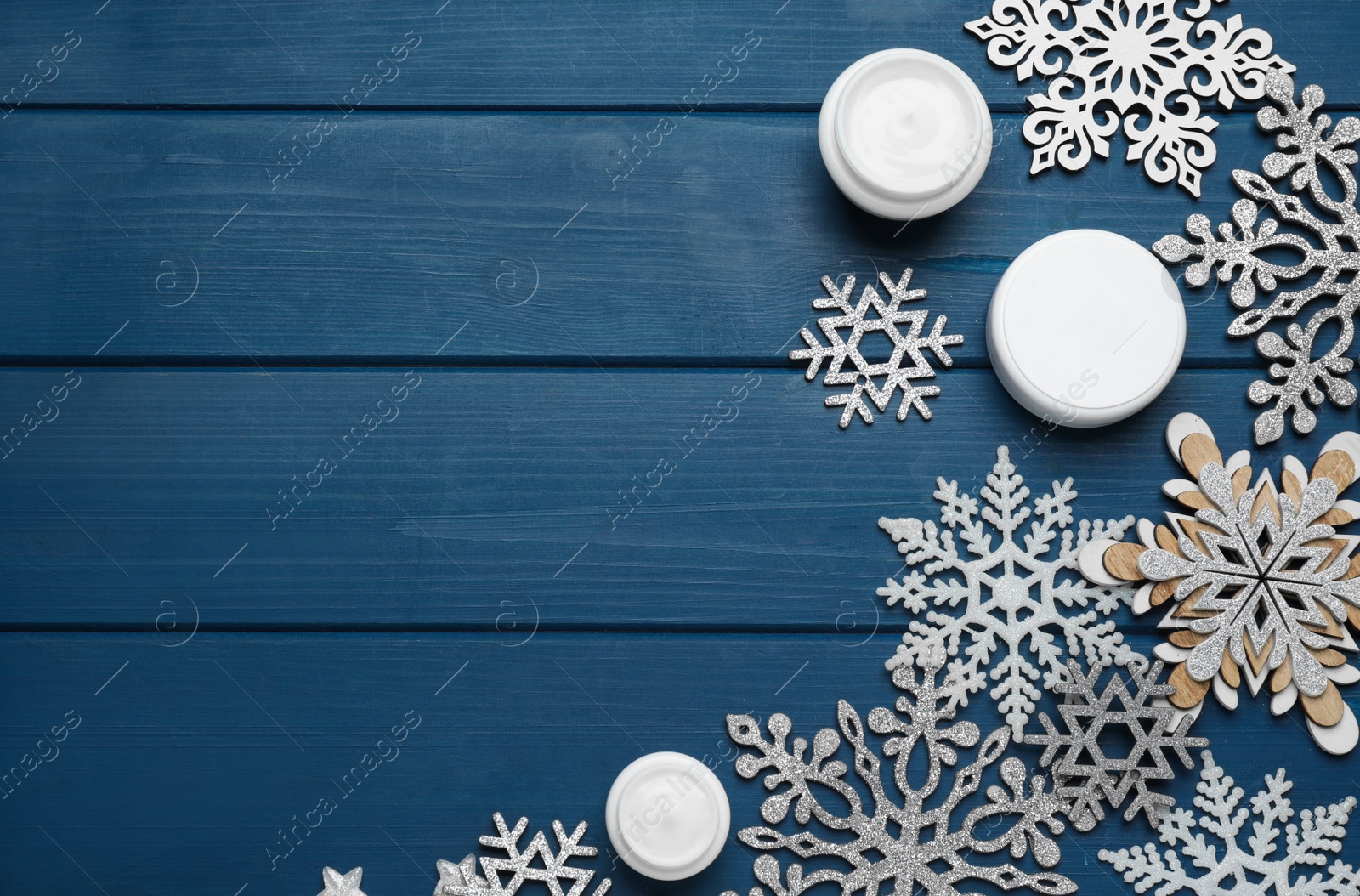 Photo of Flat lay composition with cosmetic products and snowflakes on blue wooden table, space for text. Winter skin care