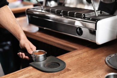 Photo of Barista holding portafilter with milled coffee on tamp mat at bar counter, closeup. Space for text