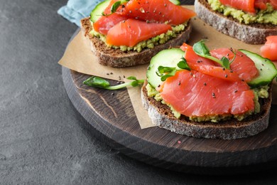 Tasty bruschettas with salmon, guacamole and microgreens on black table, closeup