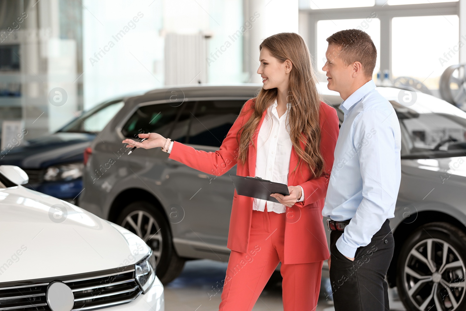 Photo of Young saleswoman working with client in car dealership