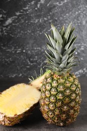 Photo of Whole and cut ripe pineapples on grey table near black wall