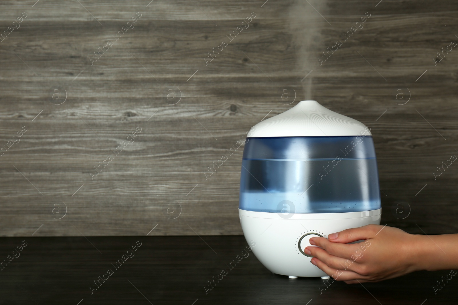 Photo of Woman using modern air humidifier at wooden table, closeup. Space for text