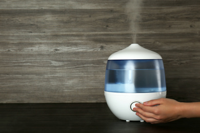 Photo of Woman using modern air humidifier at wooden table, closeup. Space for text