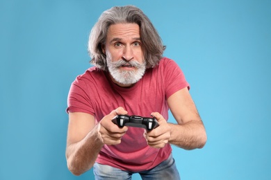 Emotional mature man playing video games with controller on color background