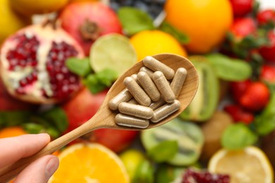 Photo of Woman holding spoon with vitamin pills over fresh fruits, top view