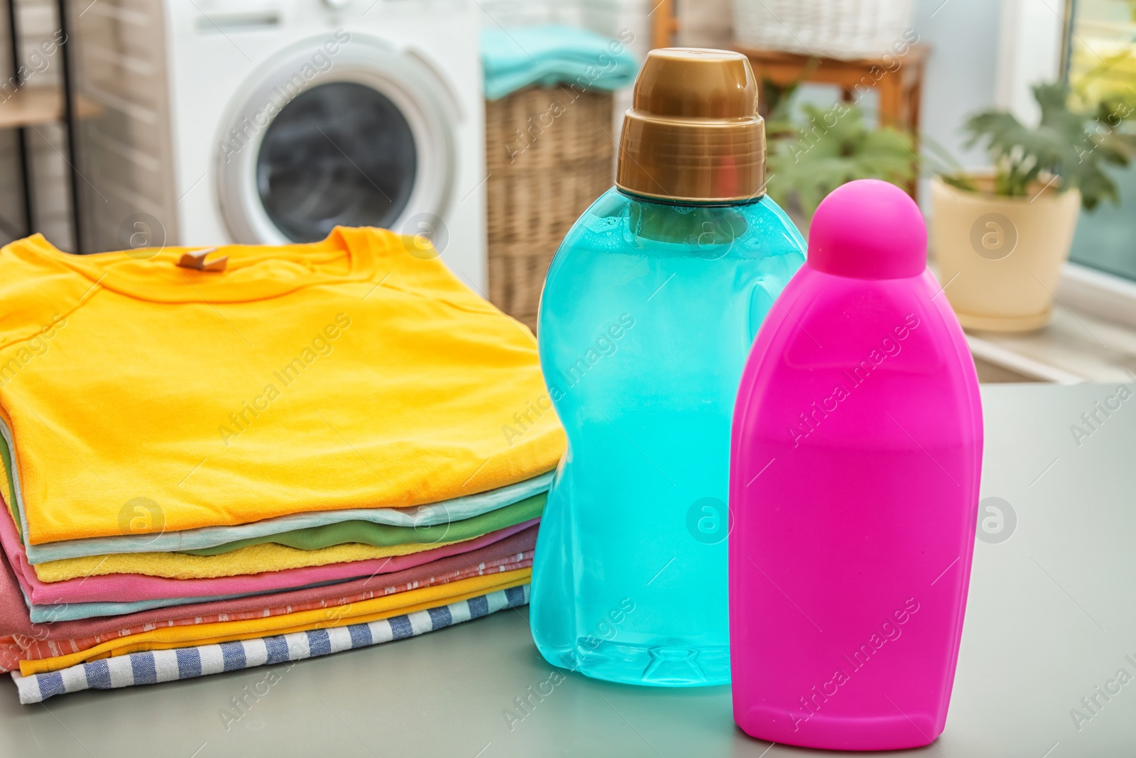 Photo of Stack of clean clothes and bottles with detergents on table in bathroom