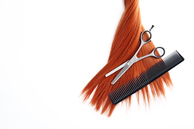 Beautiful strand of straight red hair, scissors and comb on white background, top view. Hairdresser service