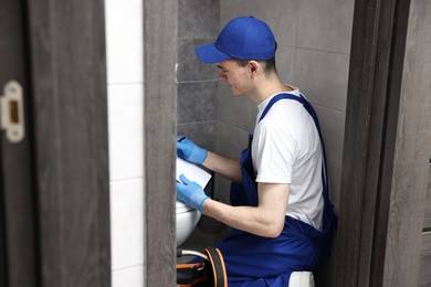 Young plumber writing results of examining toilet bowl in water closet