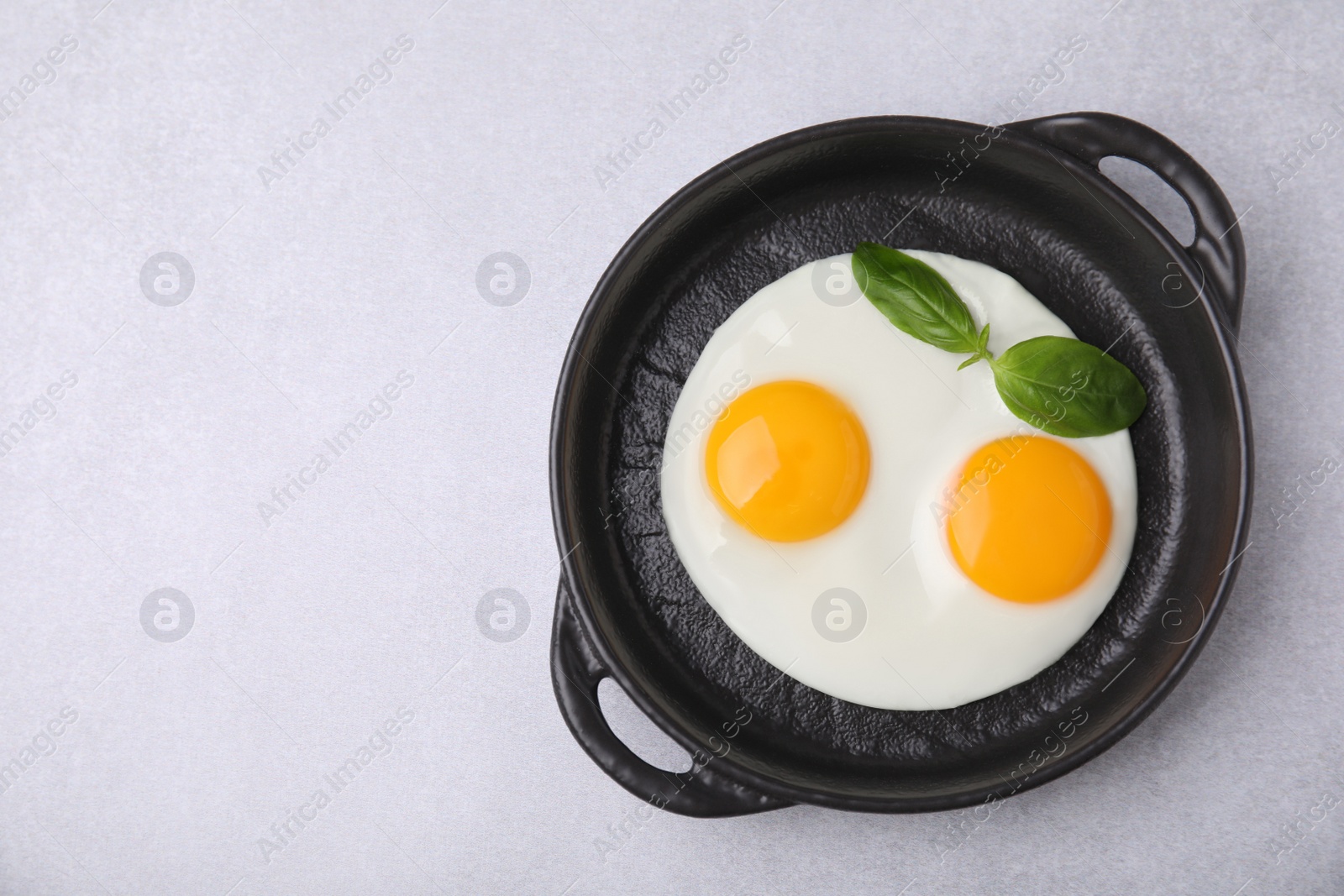 Photo of Tasty fried eggs with basil in pan on white table, top view. Space for text