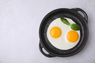 Tasty fried eggs with basil in pan on white table, top view. Space for text