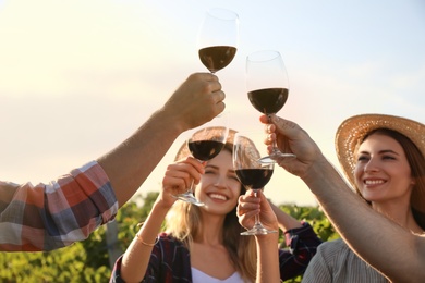 Friends clinking glasses of red wine in vineyard, focus on hands