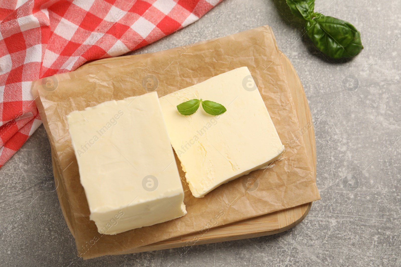 Photo of Block of tasty butter with basil on grey table, top view