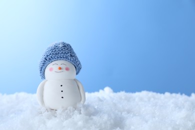 Photo of Cute decorative snowman on artificial snow against light blue background, space for text
