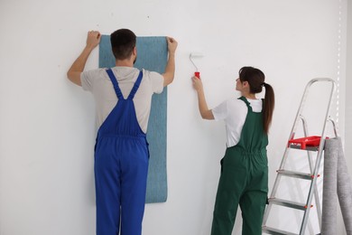 Photo of Workers hanging light blue wallpaper in room
