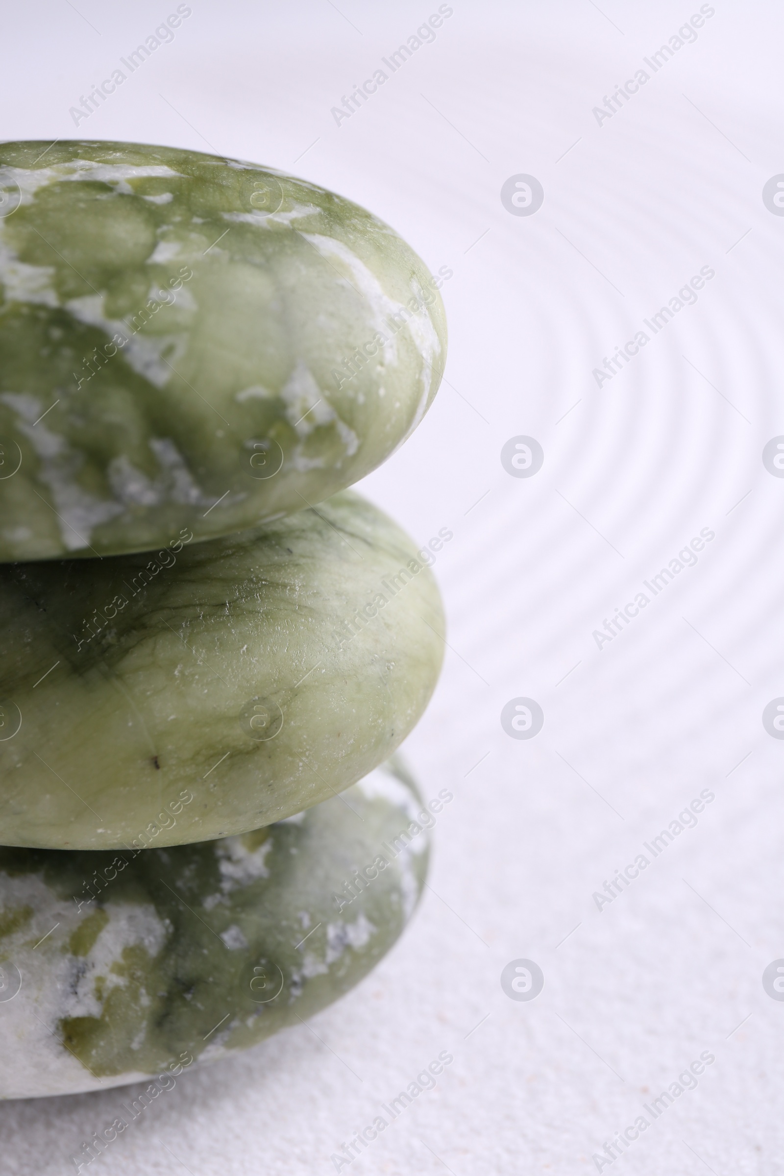 Photo of Zen garden stones on white sand with pattern, closeup