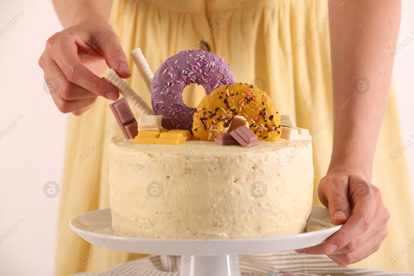 Photo of Woman decorating delicious cake with sweets on white background, closeup