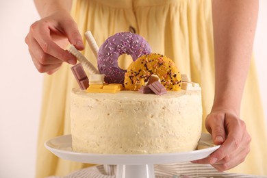 Photo of Woman decorating delicious cake with sweets on white background, closeup