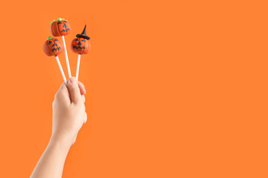 Photo of Woman with delicious pumpkin shaped cake pops and space for text on orange background, closeup. Halloween celebration