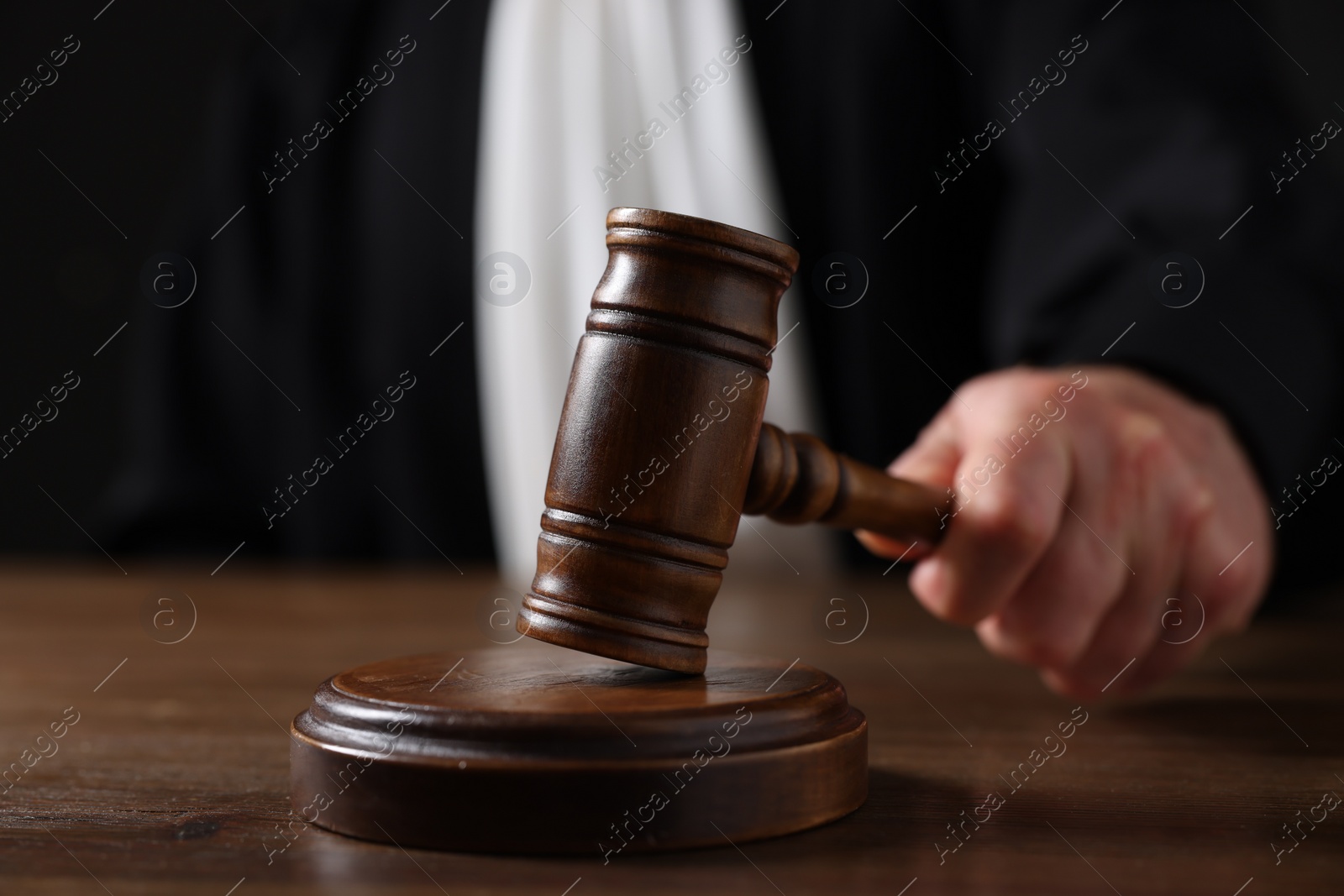Photo of Judge with gavel sitting at wooden table against black background, closeup