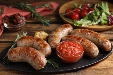 Photo of Tasty grilled sausages served with sauce on wooden table