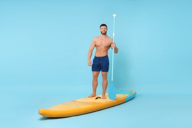 Photo of Happy man with paddle on SUP board against light blue background