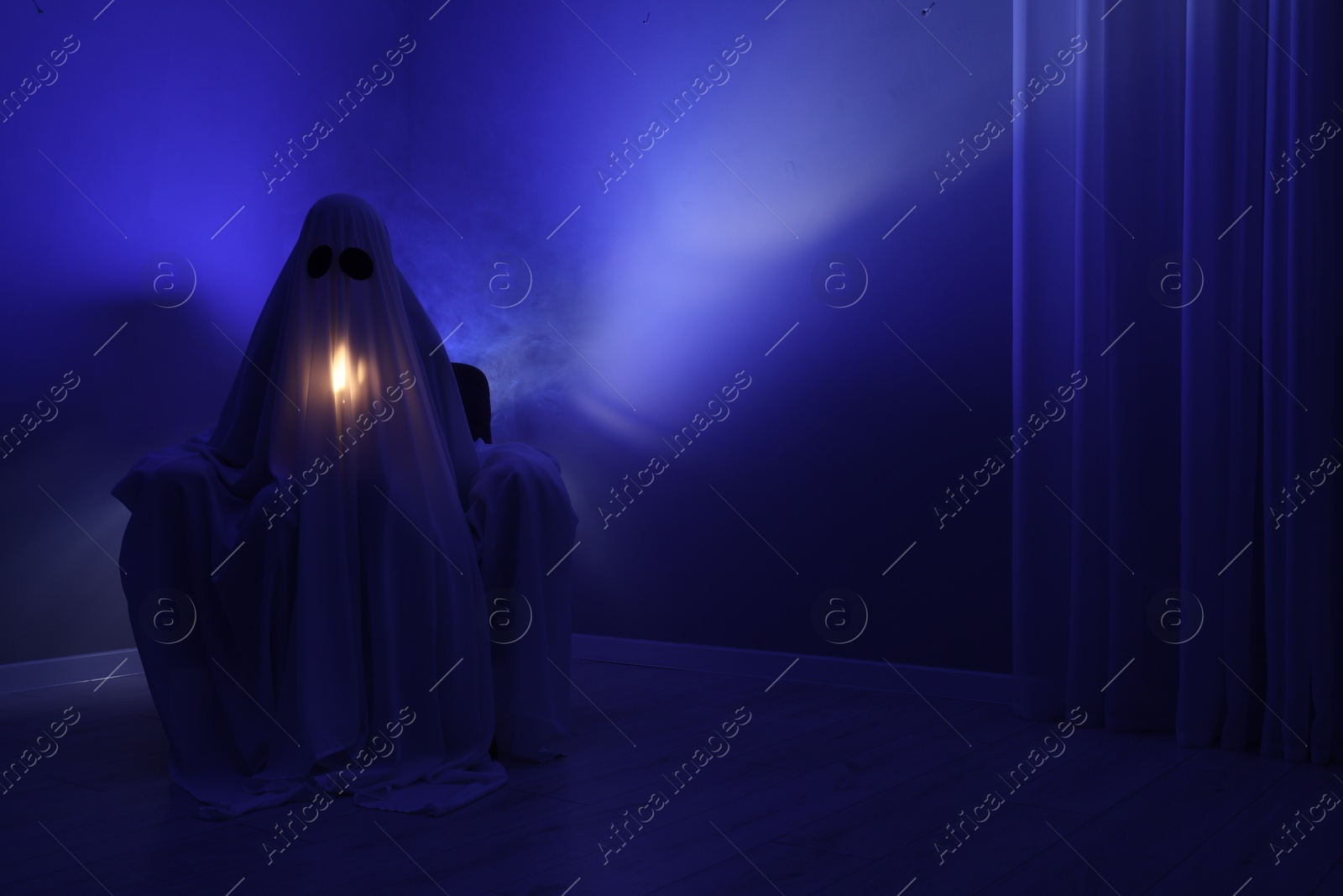 Photo of Creepy ghost. Woman covered with sheet sitting in armchair in blue light, space for text