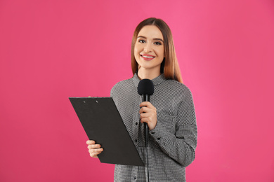 Photo of Young female journalist with microphone and clipboard on pink background