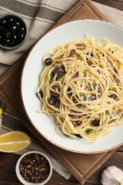 Photo of Delicious pasta with anchovies, olives and parmesan cheese served on wooden table, flat lay