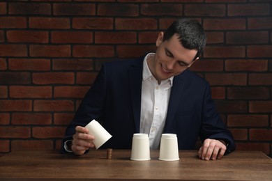 Photo of Shell game. Man showing stack of coins under cup at wooden table