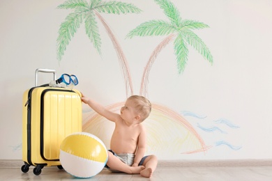 Photo of Adorable little child playing traveler with suitcase indoors
