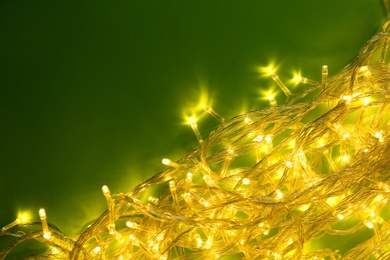 Photo of Glowing Christmas lights on green background, top view. Space for text