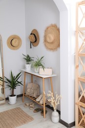 Photo of Wooden table with shoes, accessories and houseplants near white wall in hallway