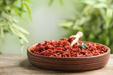 Photo of Bowl of dried goji berries on table against blurred background. Space for text