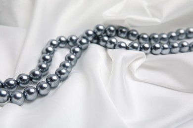 Photo of Beautiful pearls on white silk, closeup view