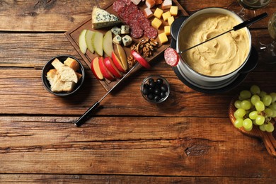 Photo of Fork with piece of sausage, melted cheese in fondue pot and other products on wooden table, flat lay. Space for text