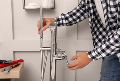 Photo of Man installing water tap with shower head in bathroom, closeup