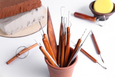 Photo of Clay and set of crafting tools on white table, closeup