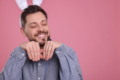 Photo of Happy man wearing bunny ears headband on pink background, space for text. Easter celebration