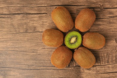 Photo of Whole and cut fresh kiwis on wooden table, flat lay. Space for text