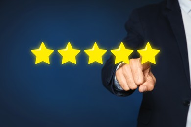 Image of Man pointing at icons of five stars on blue background, closeup. Quality rating