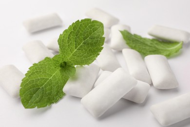 Photo of Tasty chewing gums and mint leaves on white background, closeup