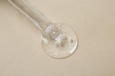 Photo of Pipette with cosmetic serum on beige background, macro view